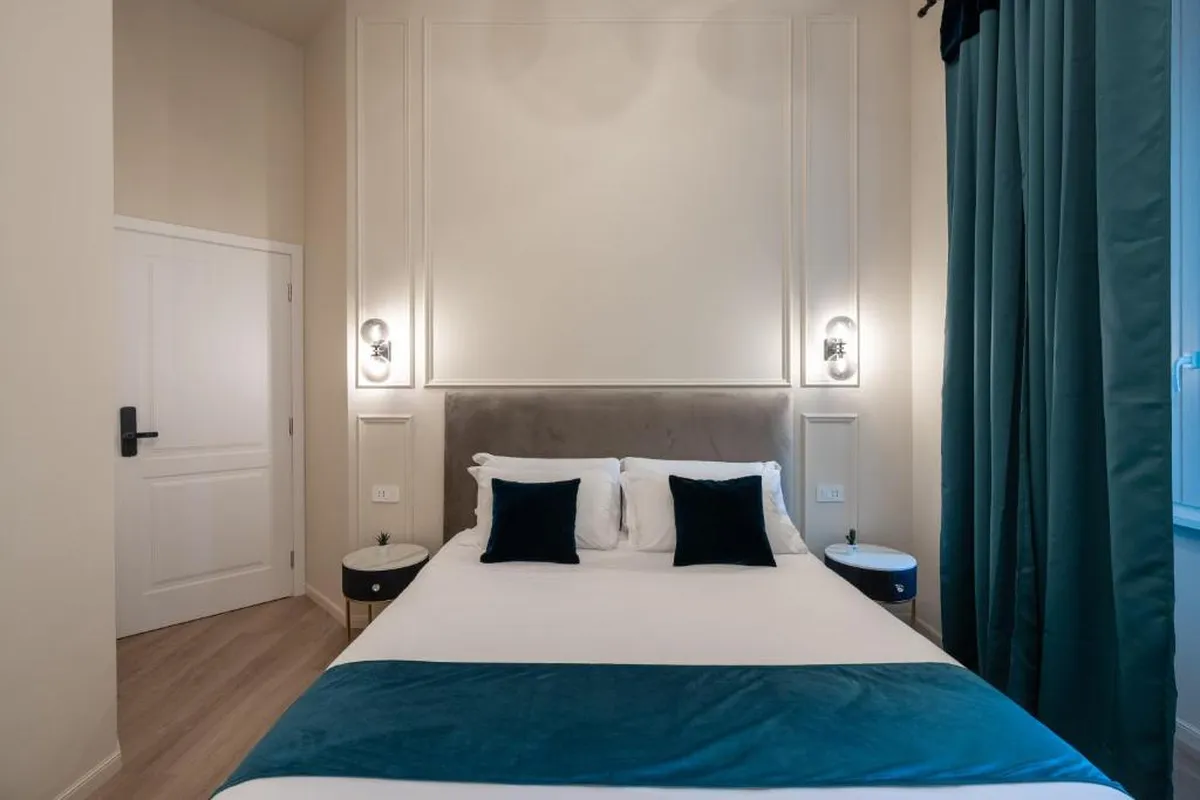 Un'altra camera dell'affittacamere all'Esquilino aperto da ReRent Group: letto matrimoniale con coperta blu petrolio e tende dello stesso colore