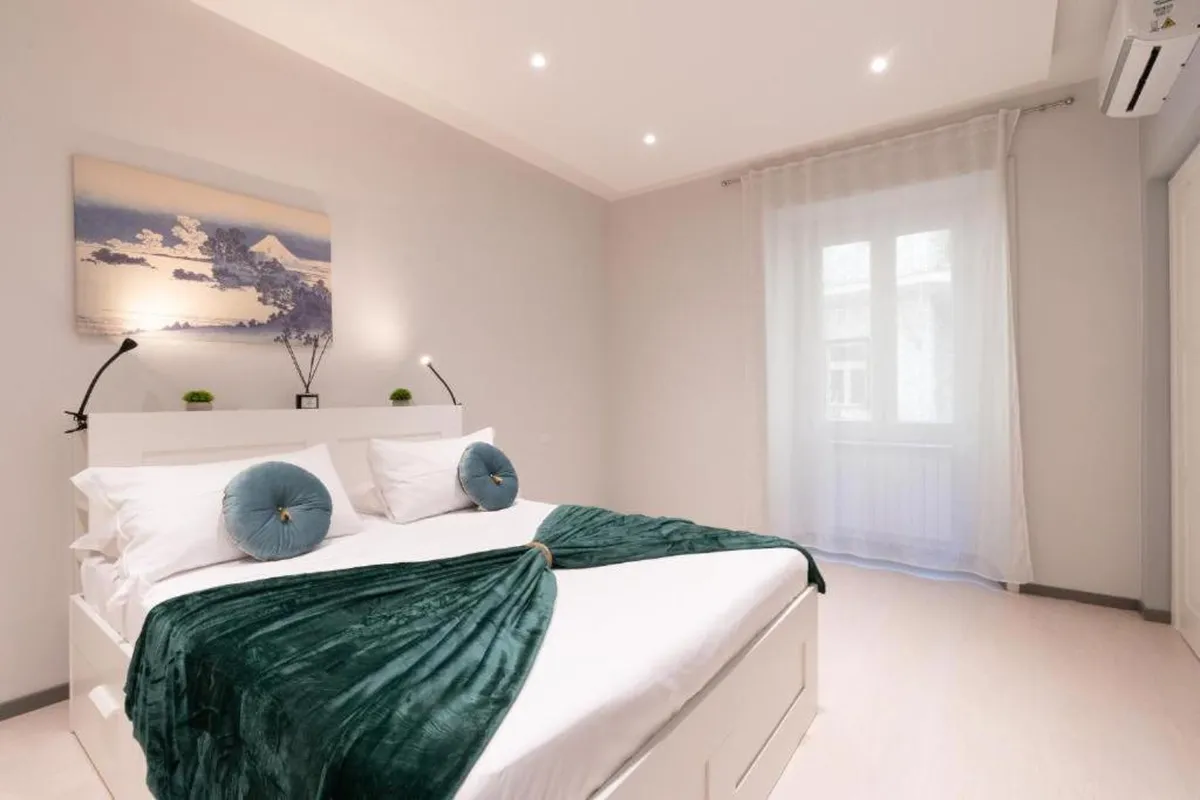 Camera da letto di un appartamento a Trastevere gestito da ReRent Group nel 2025: letto bianco, coperta verde e quadro sopra la testiera